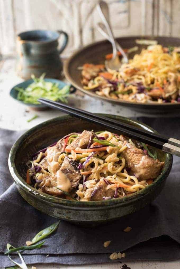 Satay Chicken Noodle Salad in a rustic ceramic green bowl with chopsticks resting on the edge, ready to be eaten.