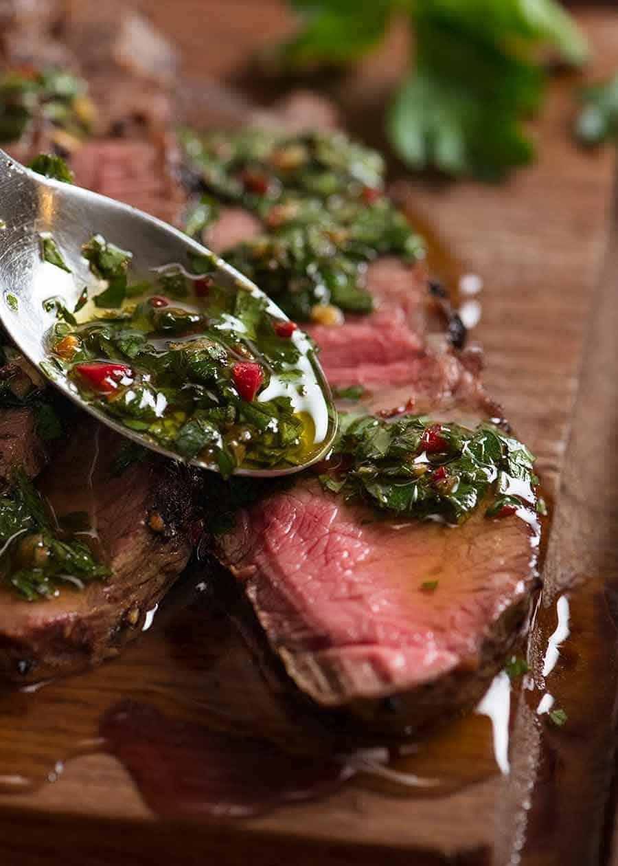 Close up of spoon drizzling Chimuchurri Sauce on steak