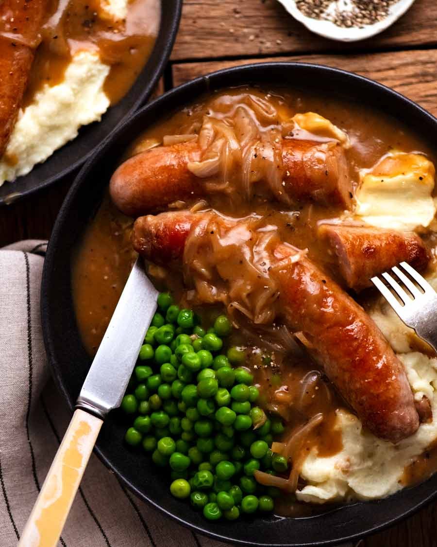 Bangers and Mash (Sausage with Onion Gravy) on a plate with mashed potato and peas