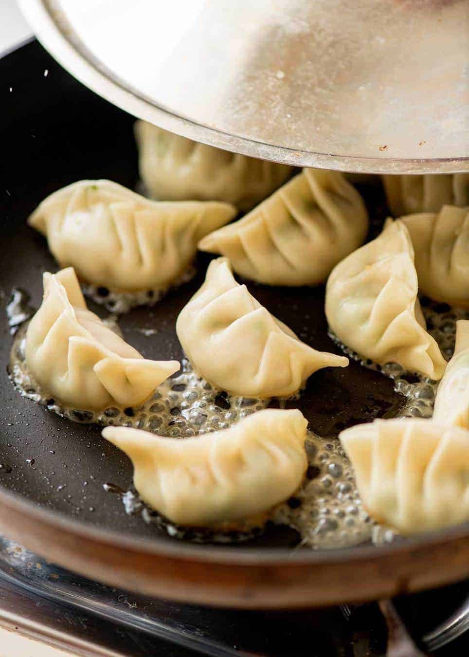Potstickers cooking in a black skillet