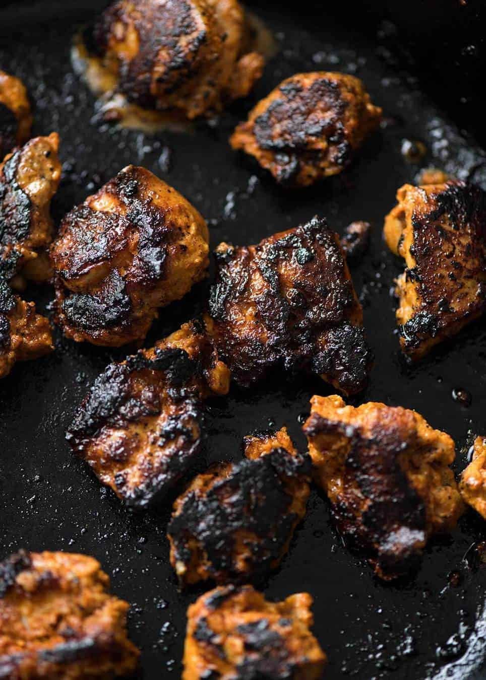 Close up of Chicken Tikka cooking in a black skillet, charred.