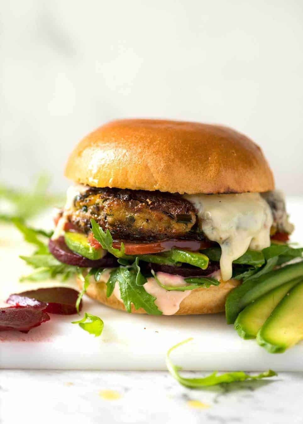 A veggie burger with melted cheese, avocado, beetroot, tomato and lettuce on a soft golden bun.