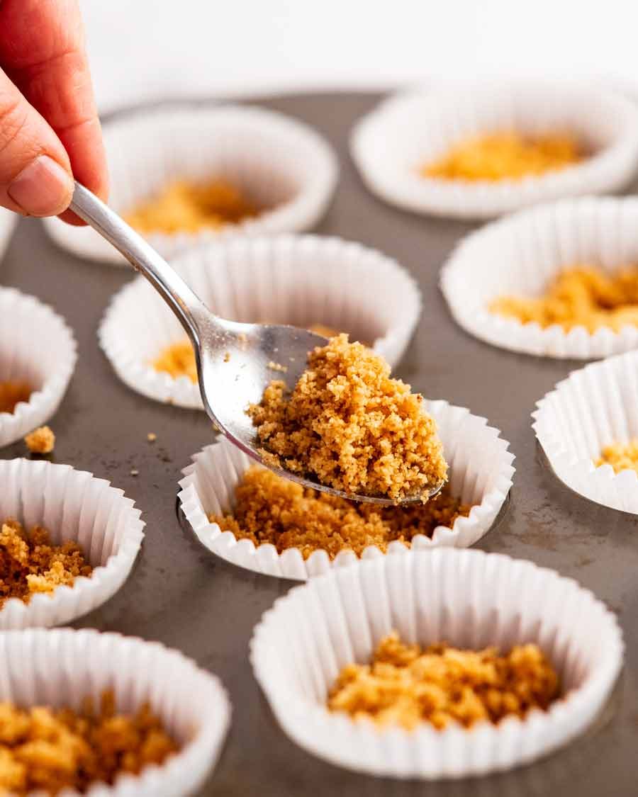 Filling muffin tin cases with biscuit base for Mini cheesecakes